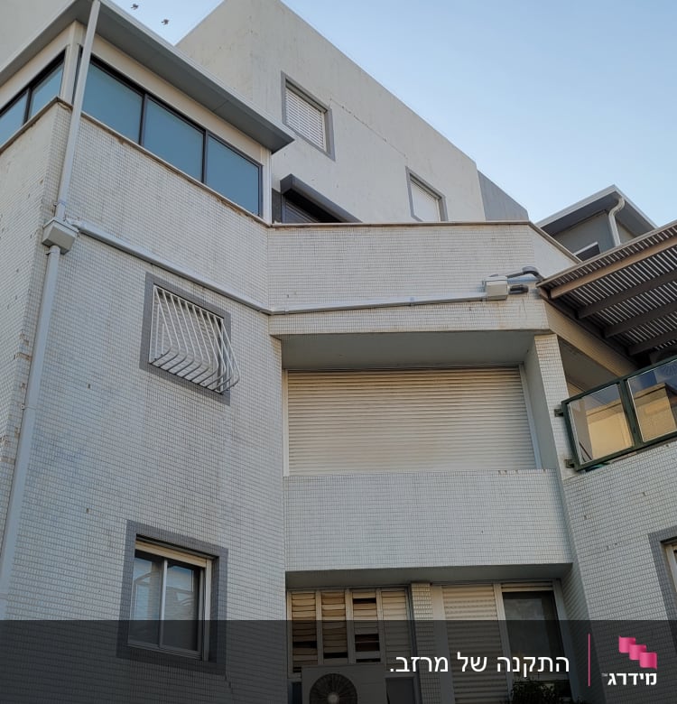 בניין עם חלונות זכוכית, תריסים ומעקות מתכת